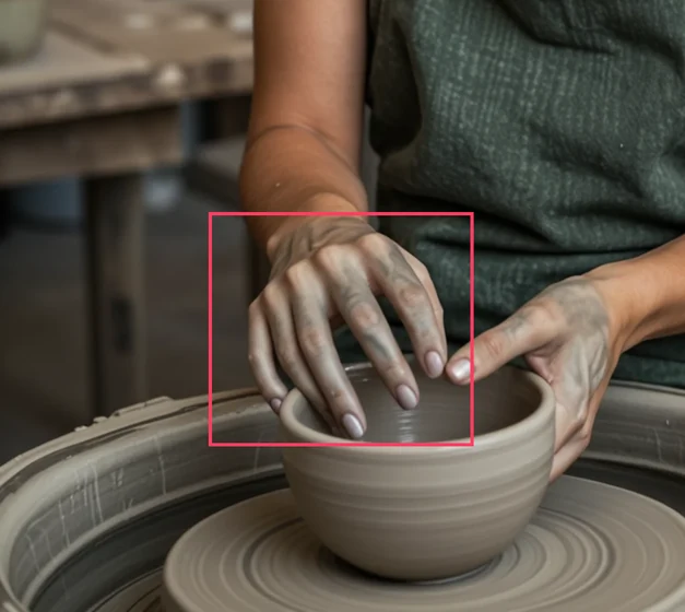 A woman shaping a bowl on a pottery wheel. The boxed hand has six fingers.